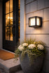 Decorative outdoor light fixture on a house exterior with a potted plant and doormat.