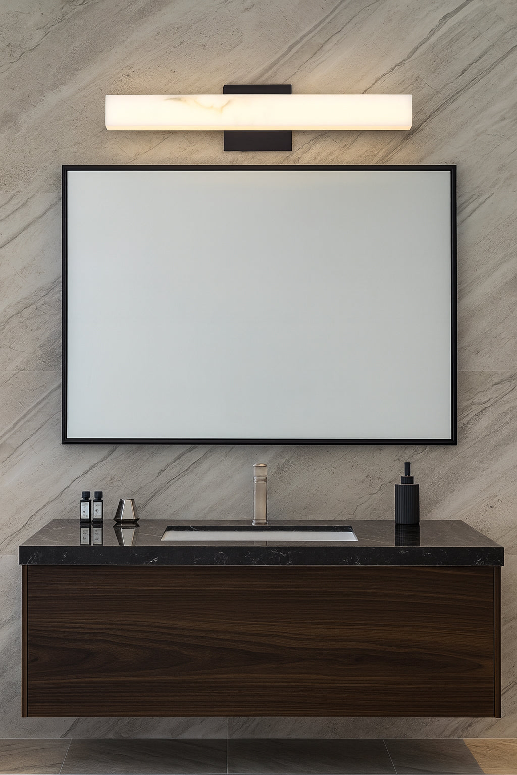 Bathroom vanity with mirror, light fixture, and toiletries against a marble wall.