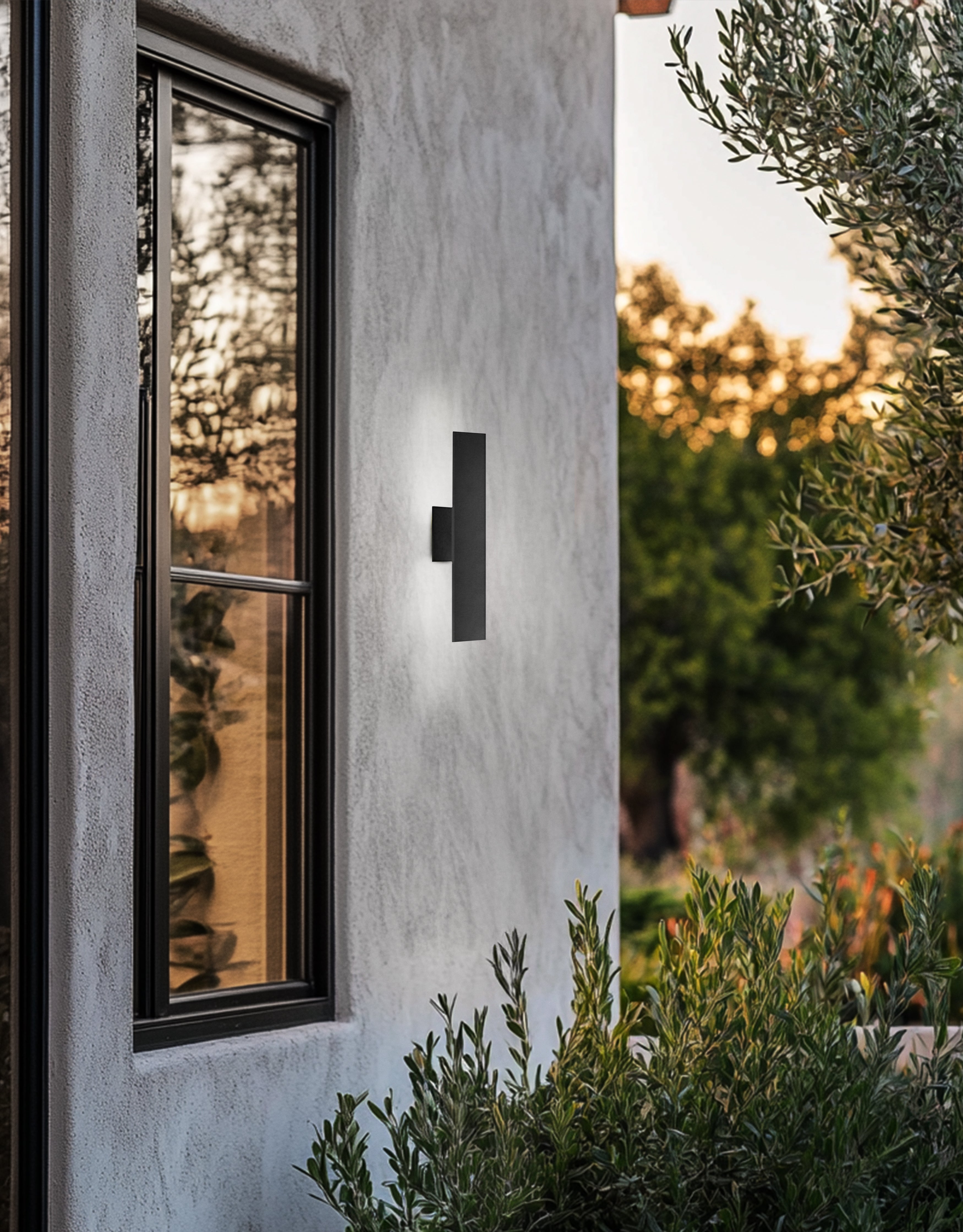 Black outdoor wall light fixture on a concrete wall with a window and garden view.