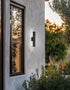 Black outdoor wall light fixture on a concrete wall with a window and garden view.
