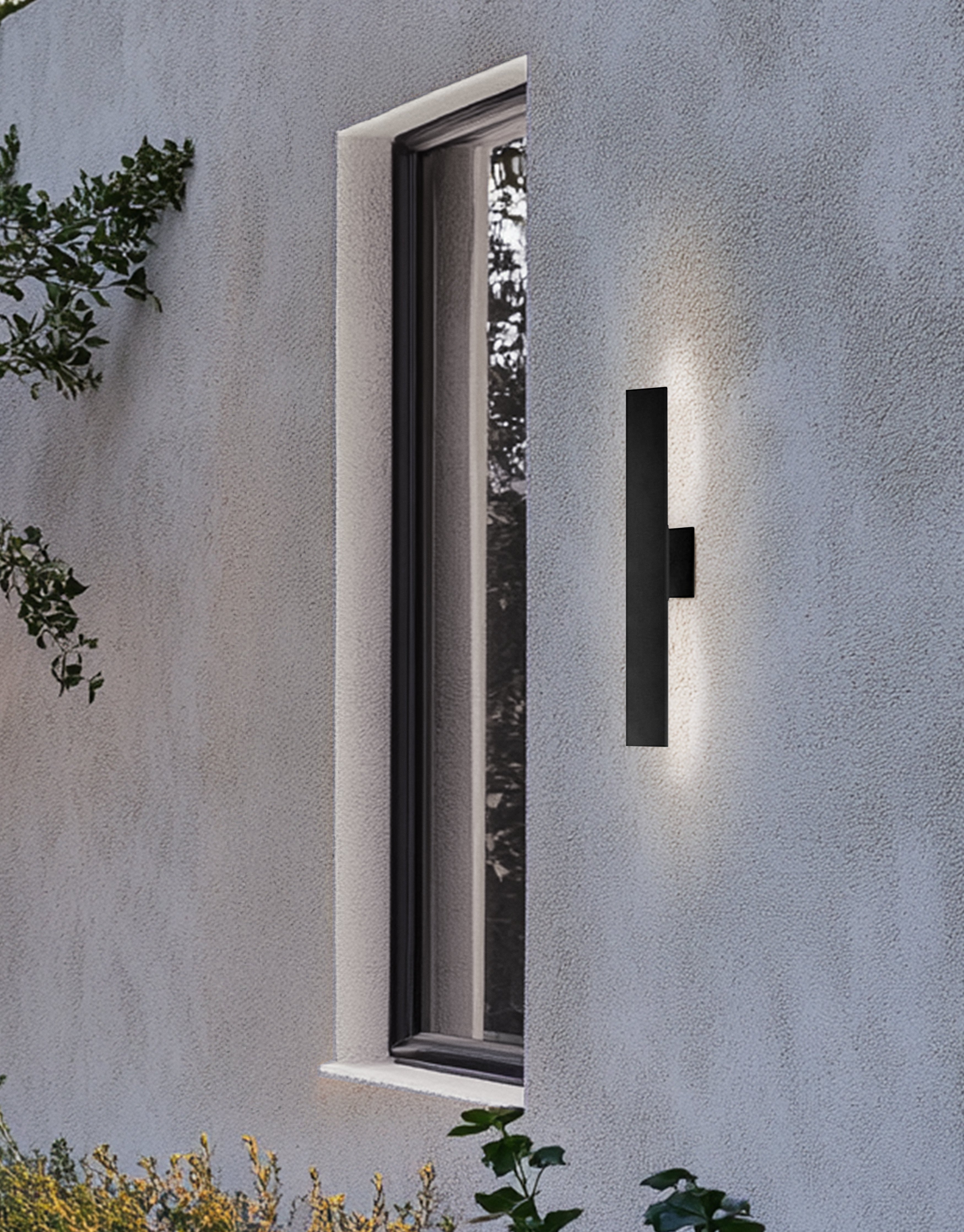 Modern outdoor wall light fixture on a concrete wall with a window and plants in the background.