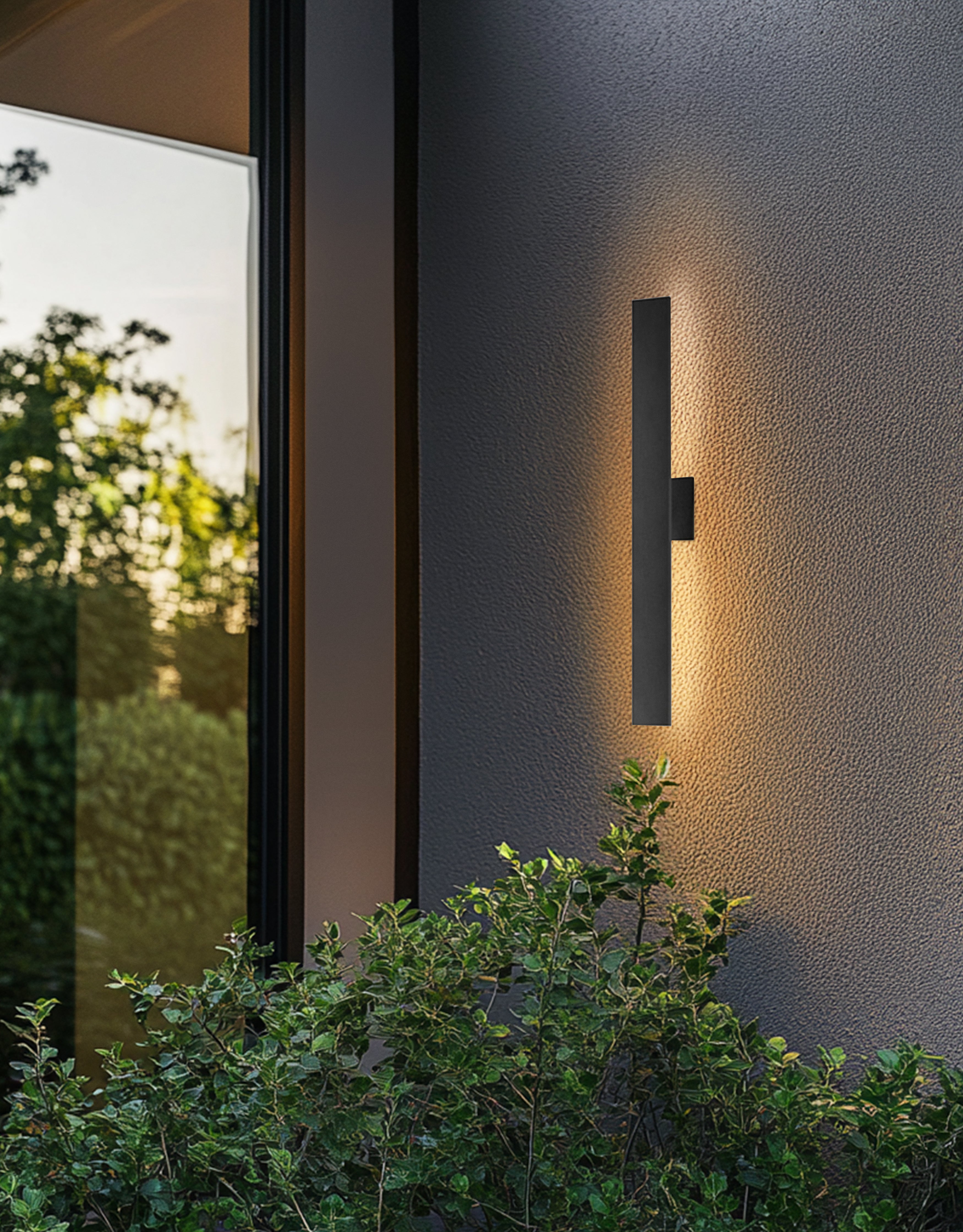 Modern outdoor wall light fixture on a textured wall with greenery in the foreground