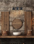 Bathroom with wooden vanity, round mirror, and light fixture on stone wall.