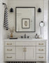 Bathroom vanity with mirror, sink, and decorative items against a white tiled wall.
